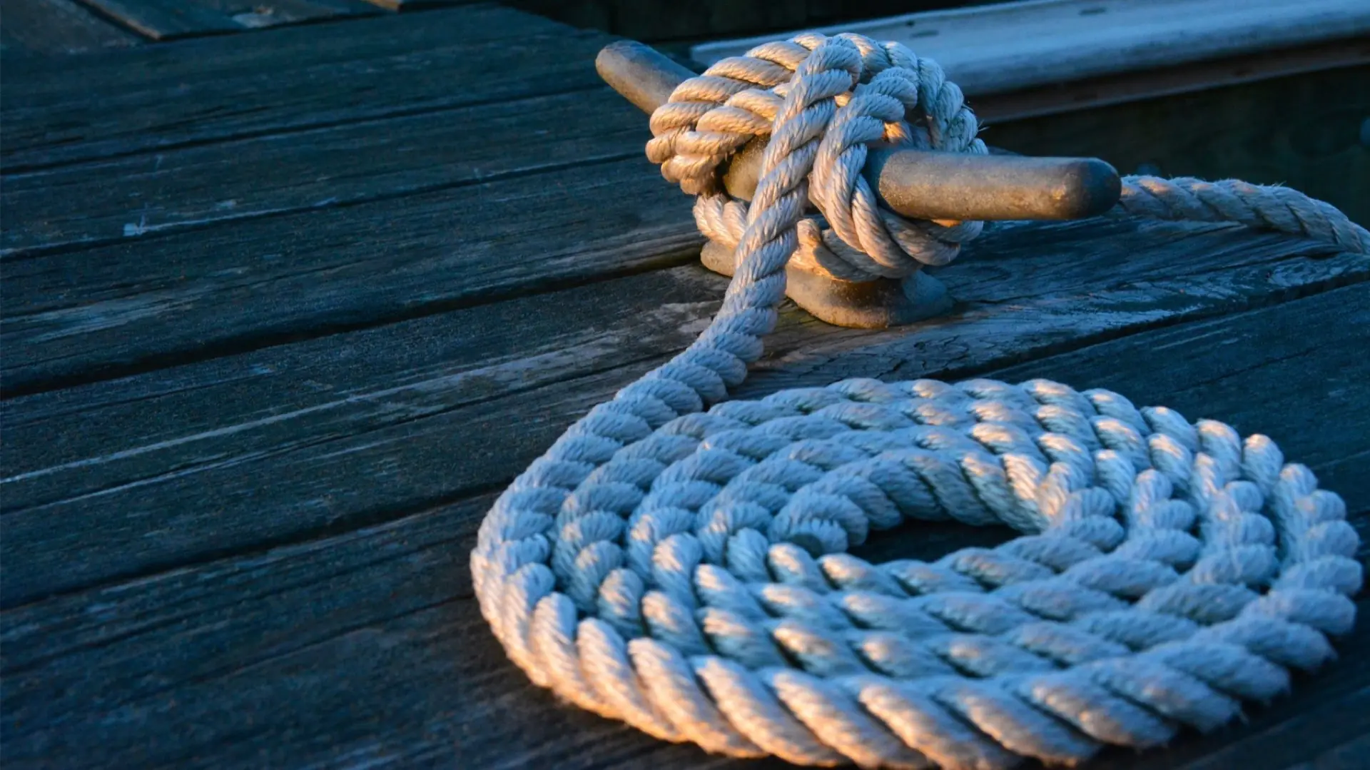 A mooring line made fast to a cleat and coiled on a weathered wooden pontoon in evening light