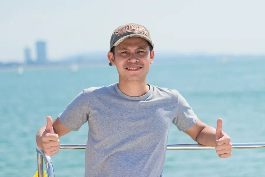 A man on deck giving a thumbs up in front of turquoise water
